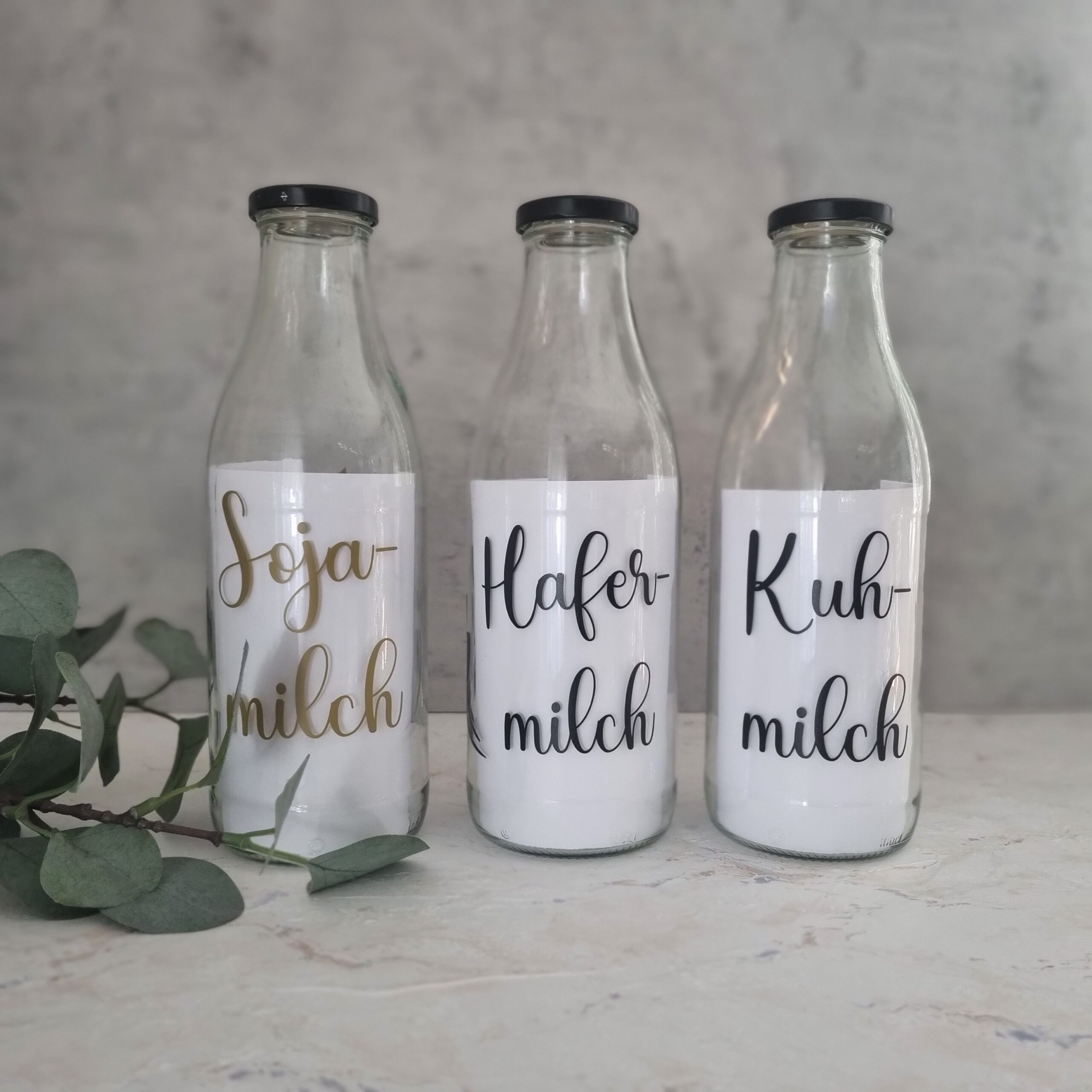 Vier Glasflaschen aus Recyclingglas mit Beschriftung „Goldene Milch“, „Mandelmilch“, „Sojamilch“ und „Hafermilch“ – wiederverwendbar und nachhaltig.